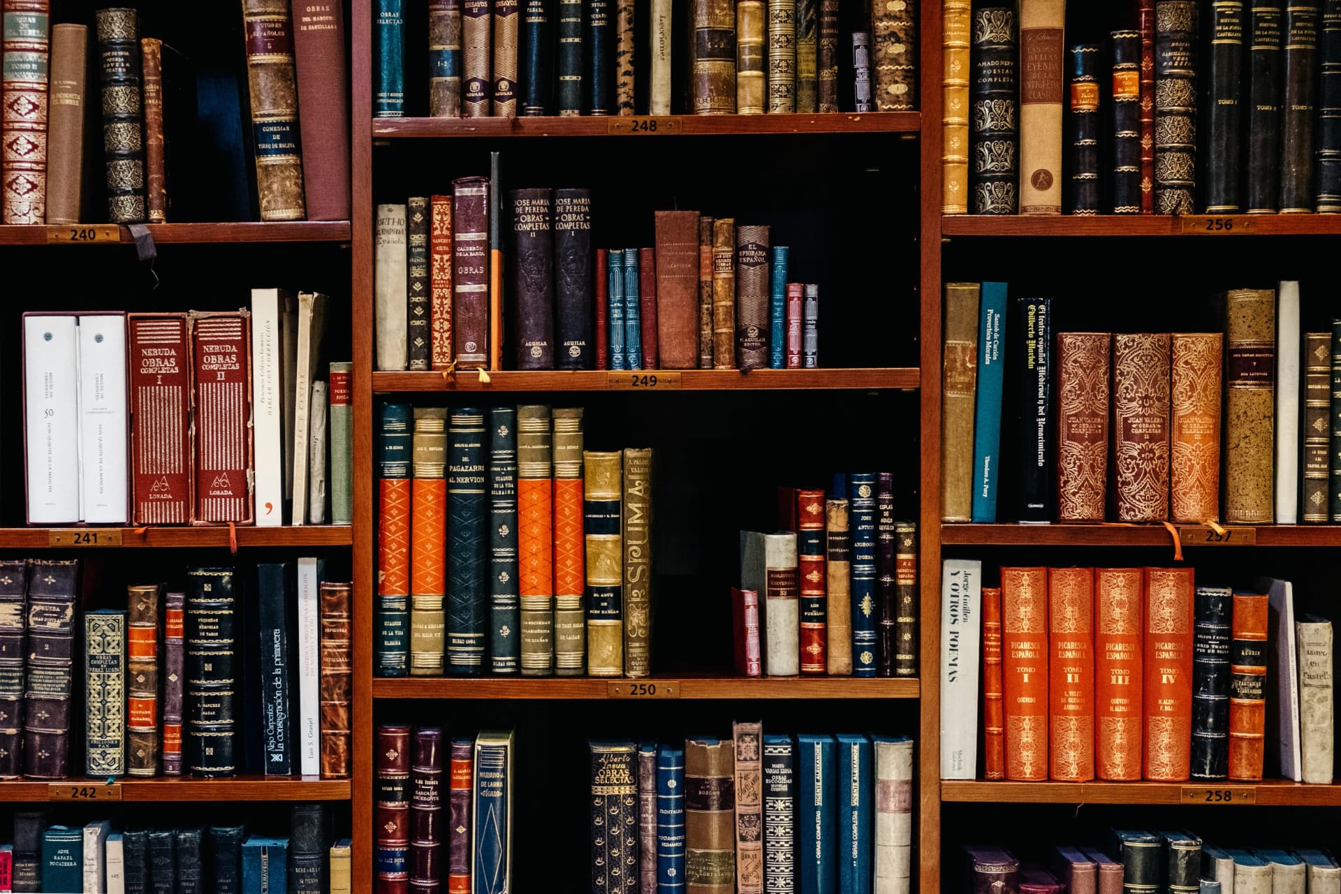Wooden library shelves filled with rows of old leather-bound books with numbered shelf labels