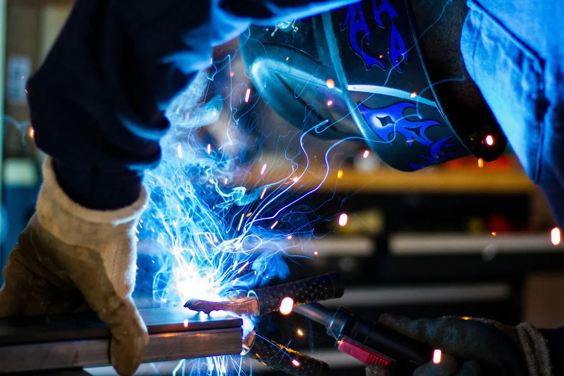 Welder in a decorated helmet and gloves welding a metal part as blue-white sparks fly