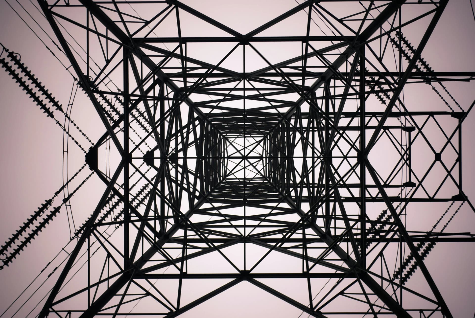Looking straight up through the steel lattice framework of an electricity pylon, with insulators and power lines on each side