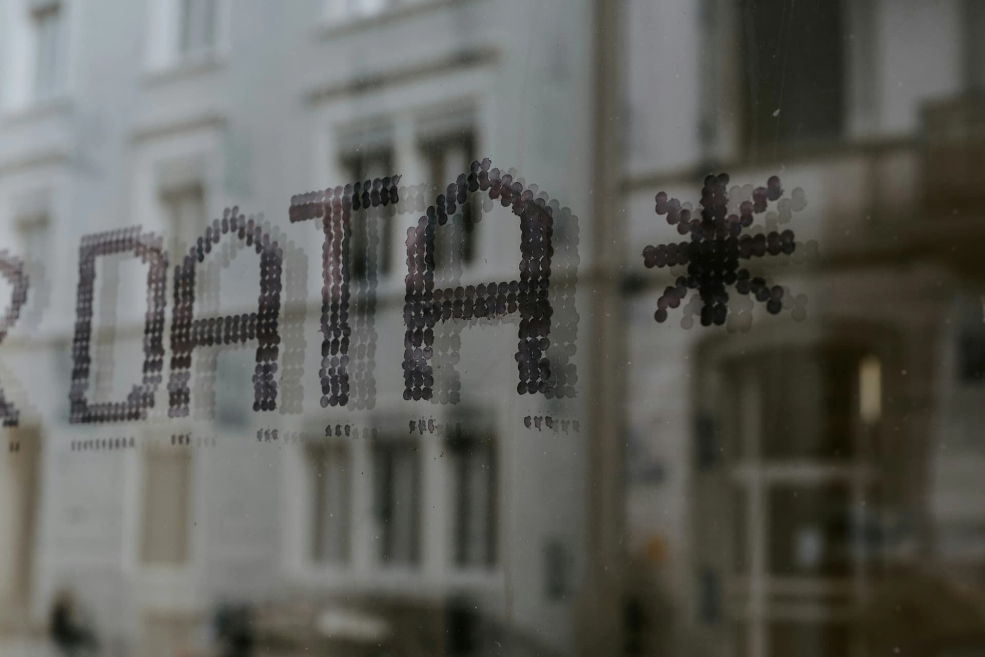 The word DATA and an asterisk printed in dotted letters on a window, with a blurred building facade behind the glass